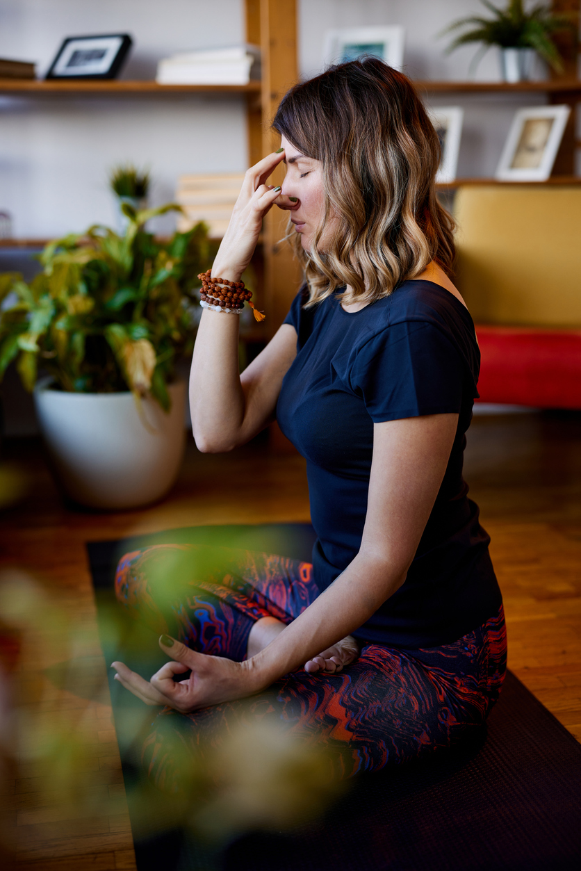 A yogi woman is sitting on a yoga mat in the lotus position and doing breathing exercises.